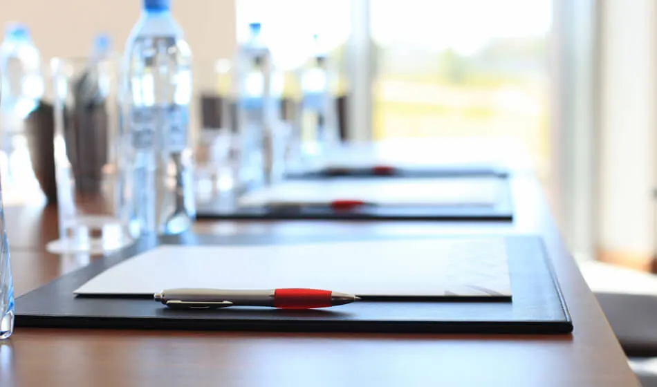 Conference table with water bottles and notepads laid out in a bright meeting room with windows.