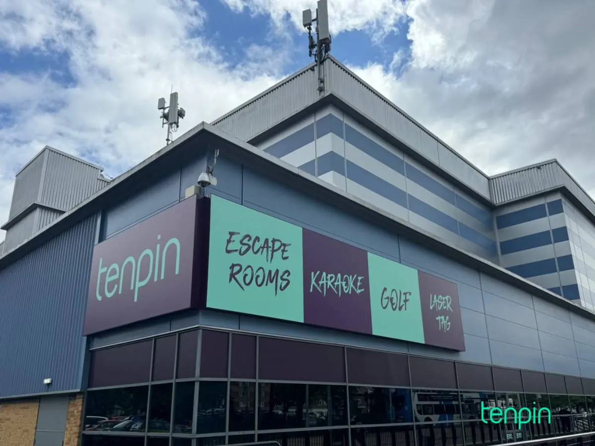 Modern leisure venue building with signage advertising escape rooms, karaoke, golf and laser tag against cloudy sky.