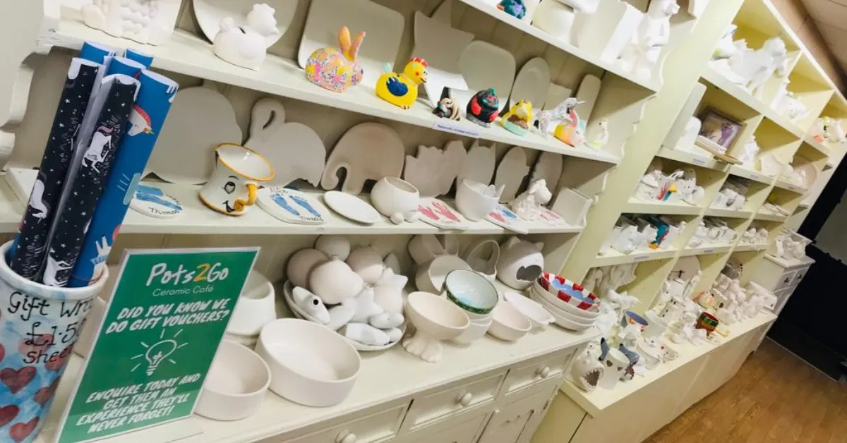 Shelves displaying unpainted ceramic pieces including bowls, mugs, animal figurines and decorative items available for painting at a pottery studio.