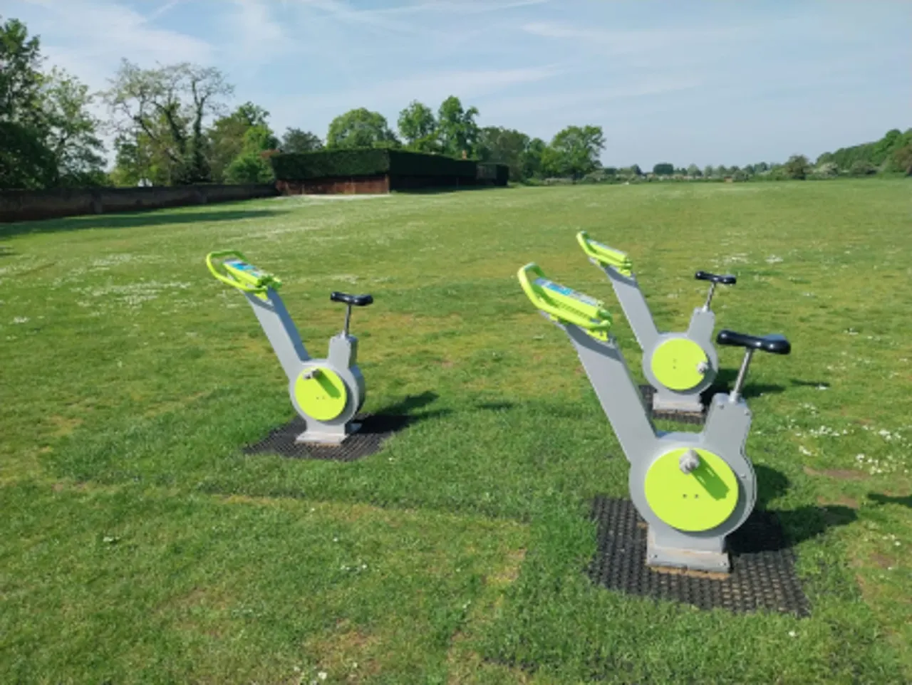 Outdoor fitness equipment arranged across a grassy field with trees and farm buildings in the background.