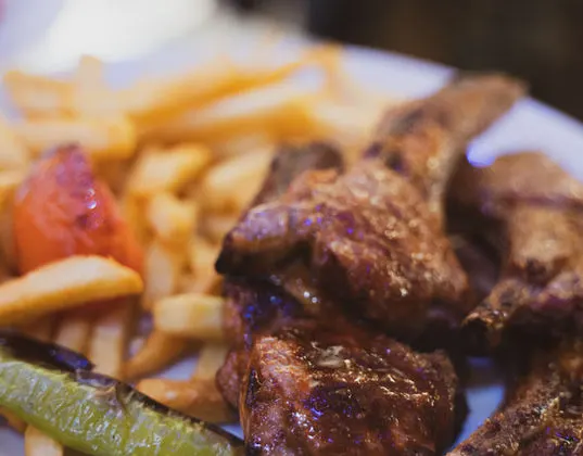 Grilled meat skewers with chips, tomato and pepper on a white plate.