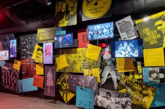 Exhibition wall at Strawberry Field featuring photographs, memorabilia and yellow and coloured information panels about John Lennon.