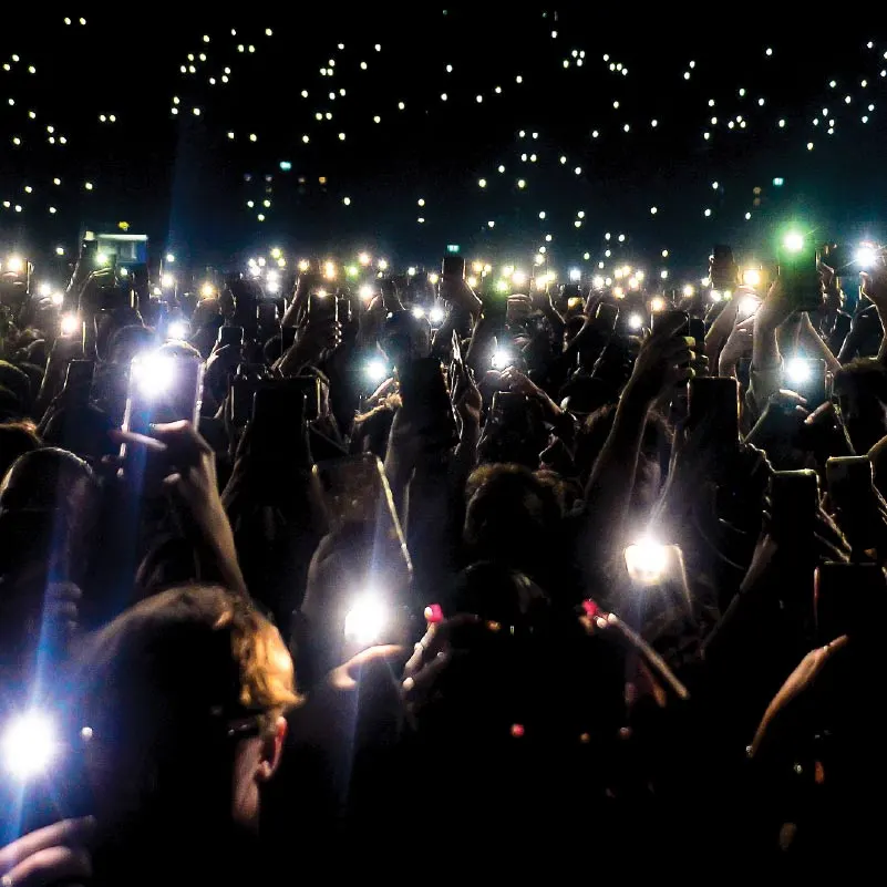 Arena crowd holding phone lights during a concert.