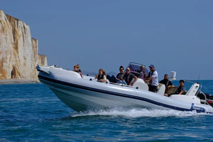 Group of visitors on a speedboat approaching white chalk cliffs on a sunny day at sea.