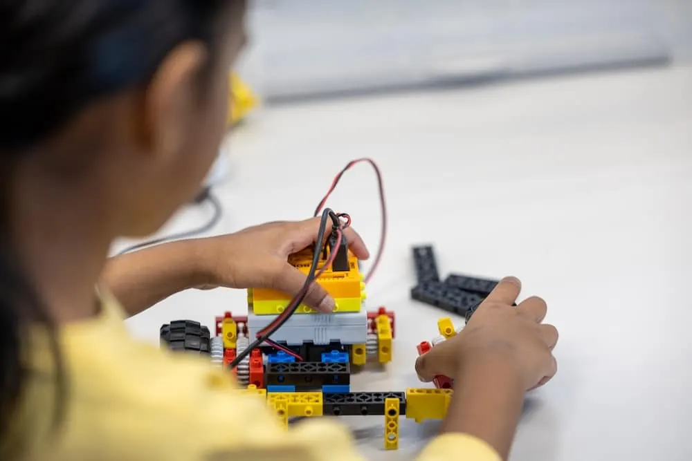 Child in yellow shirt building and connecting wires to a colourful plastic brick construction project.