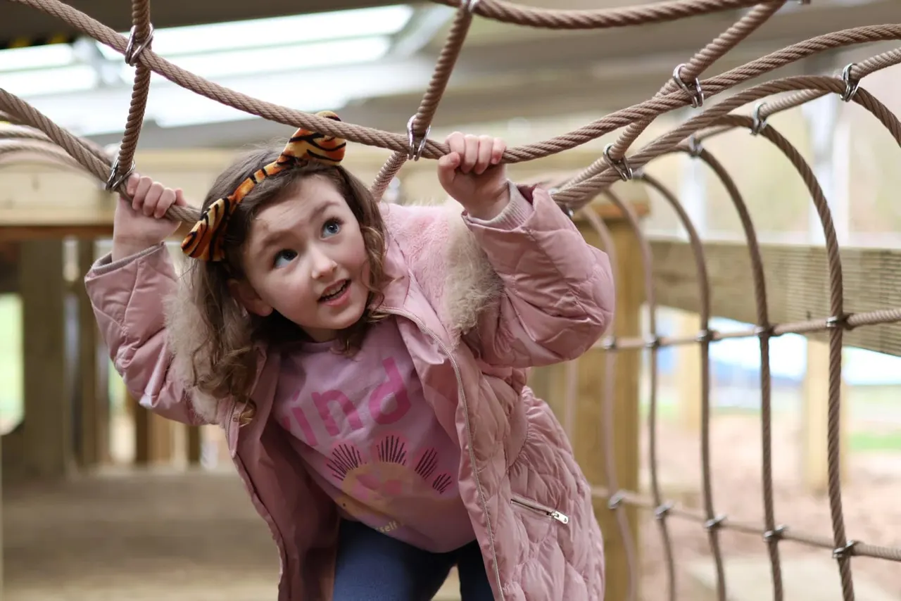 Young child swinging from rope in an indoor play area.