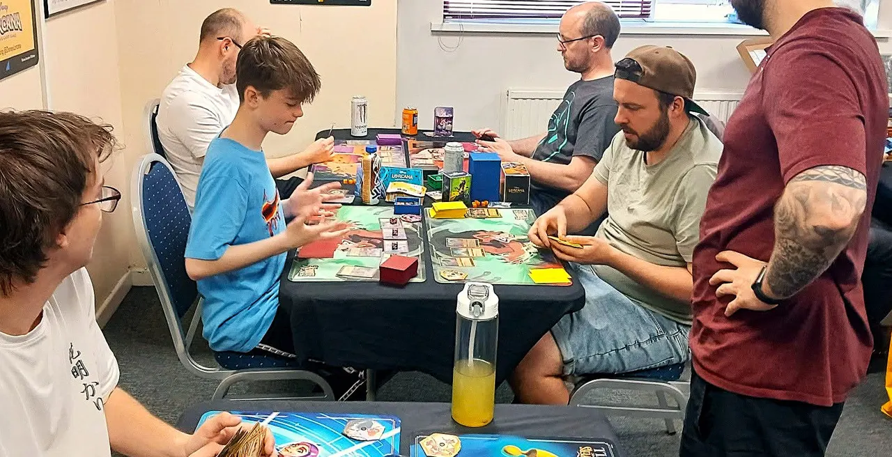 A group of adults and children gathered around a table playing board games together indoors.