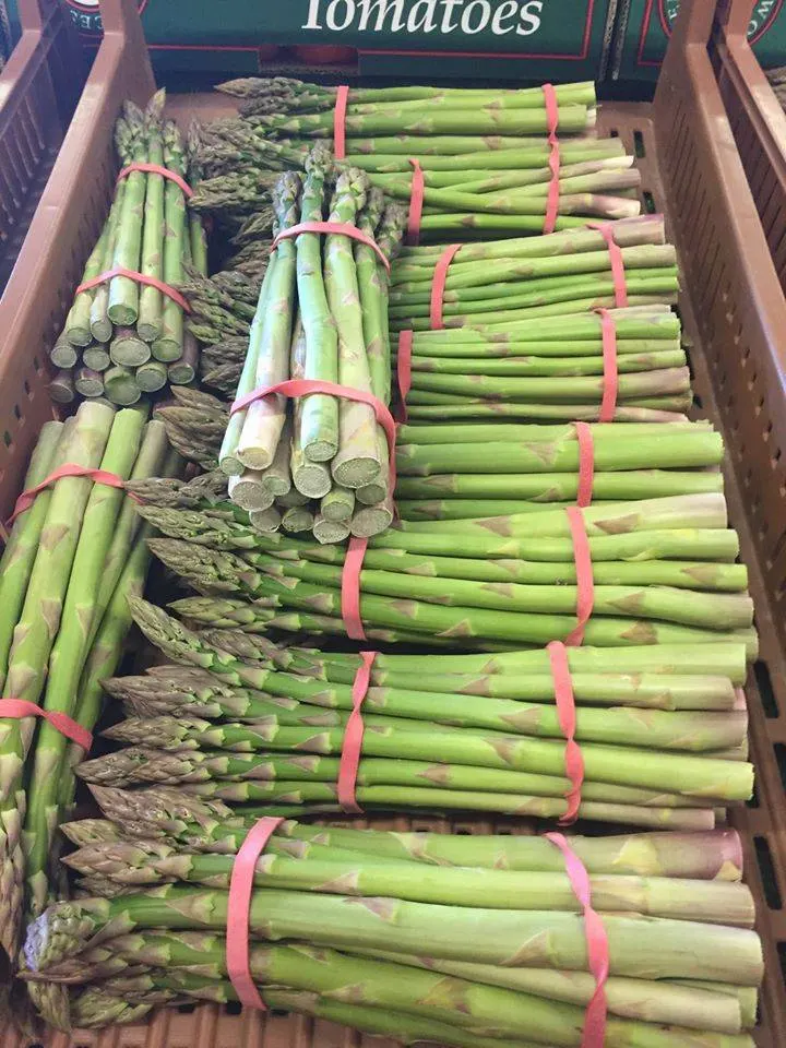 Fresh asparagus bundles tied with pink bands displayed in wooden crates at a farm shop.