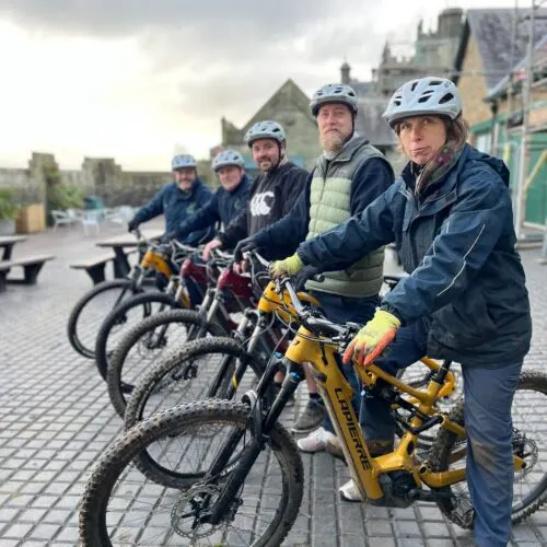 A line of people wearing helmets standing with yellow bikes in front of a castle, ready for a cycling activity.
