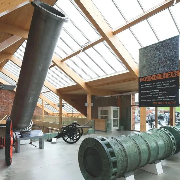 Historic artillery pieces displayed in a modern museum gallery with glass roof and wooden beams.
