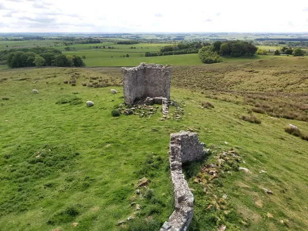 Aerial view of stone ruins on moorland with pastoral countryside and forests stretching to the distant horizon.