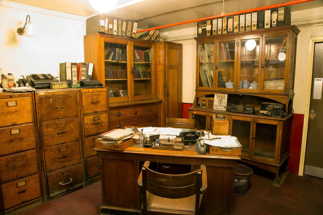 A recreated vintage office interior with wooden desks, filing cabinets, typewriters and period furnishings displayed in a museum setting.