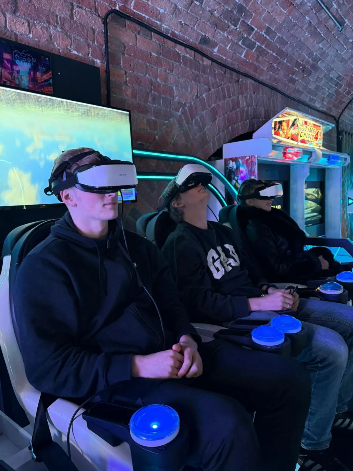 Three people wearing VR headsets and holding controllers sit in a row, engaged in a virtual reality gaming experience.