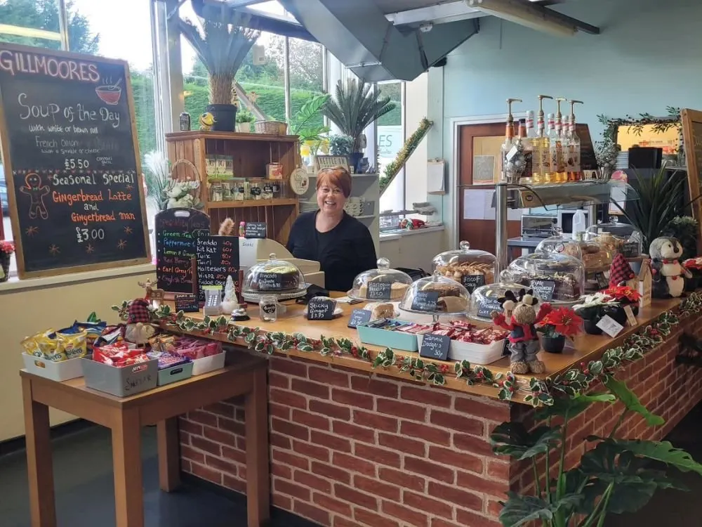 Staff member stands behind a bakery counter displaying festive baked goods and seasonal treats at a garden centre café.