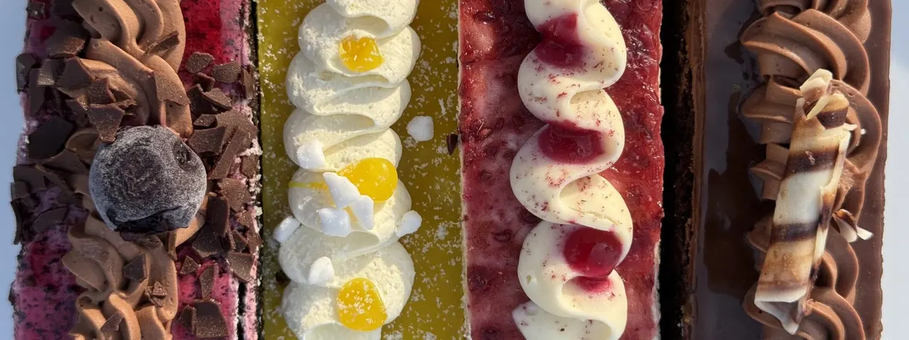 Array of decorative cakes and pastries in chocolate, pistachio, lemon and berry flavours with cream toppings and garnishes.