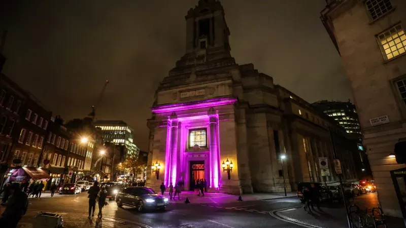 Historic stone building with classical architecture illuminated in magenta pink lighting at night, with surrounding Georgian streetscape and traffic.