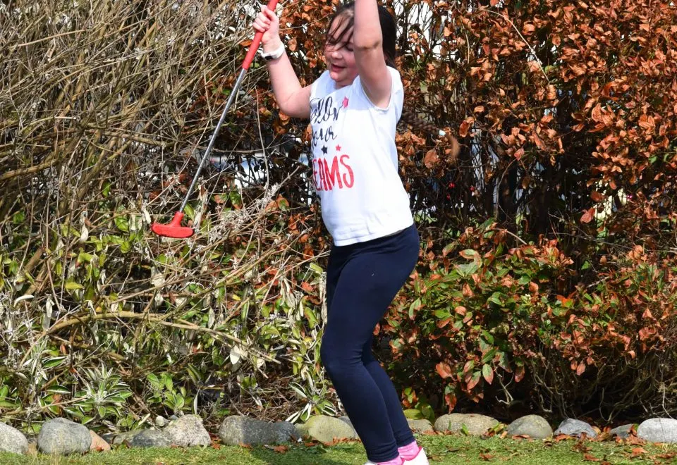 A child swinging on a rope swing with a red handle against a backdrop of autumn foliage and hedging.