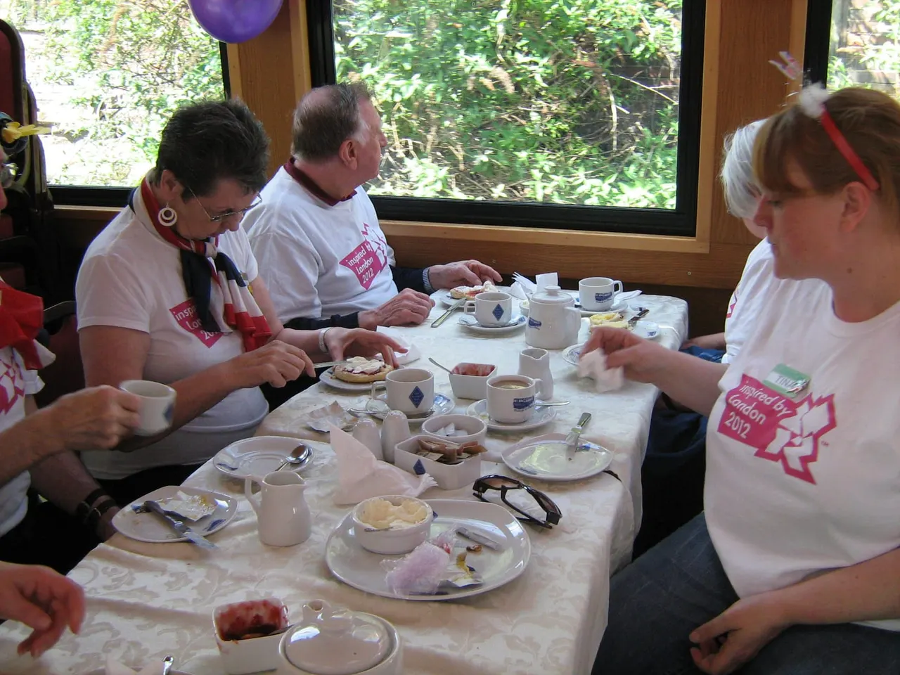 Guests enjoy afternoon tea at a table inside a cabin with large windows overlooking green foliage.