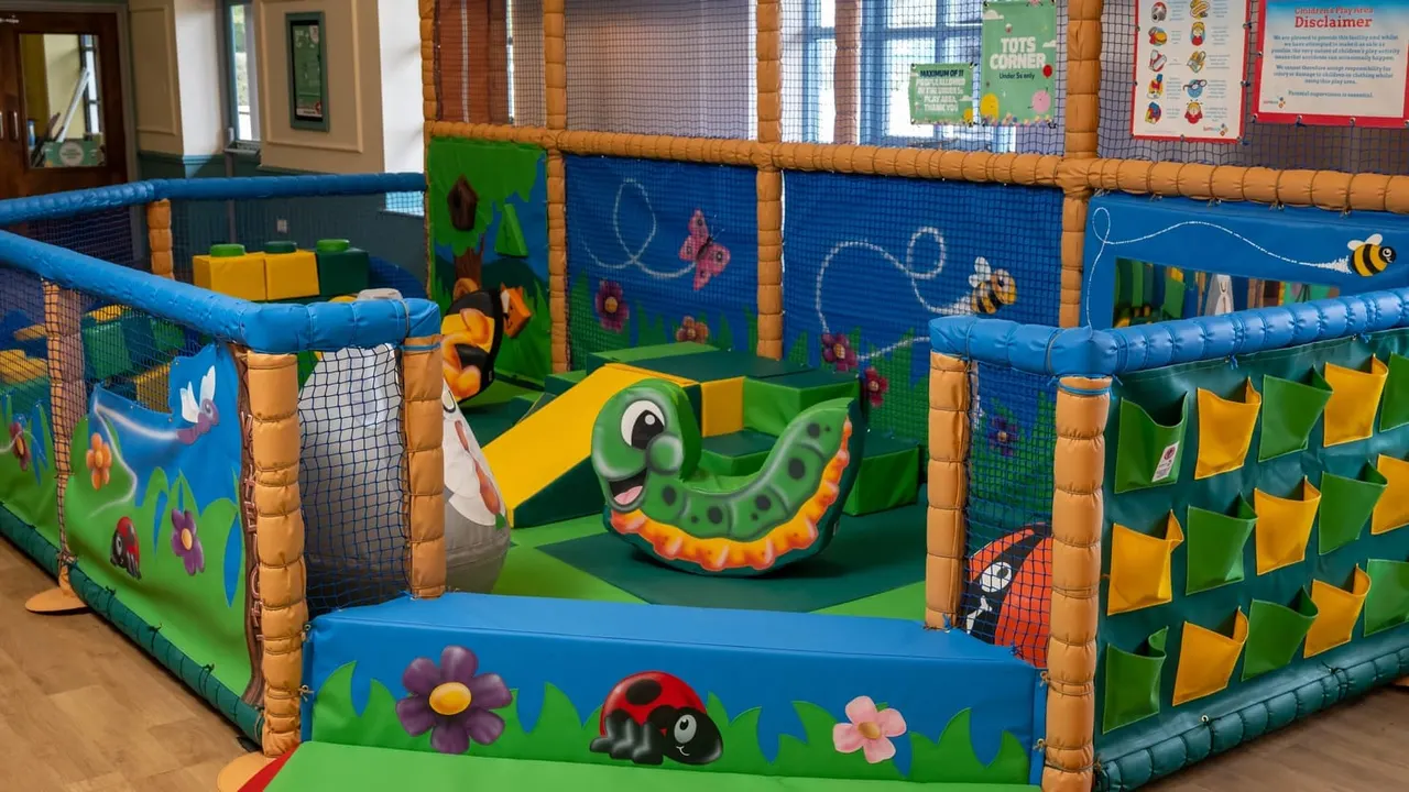 Colourful soft play area with inflatable structures decorated with insects, flowers and garden themes for young children.