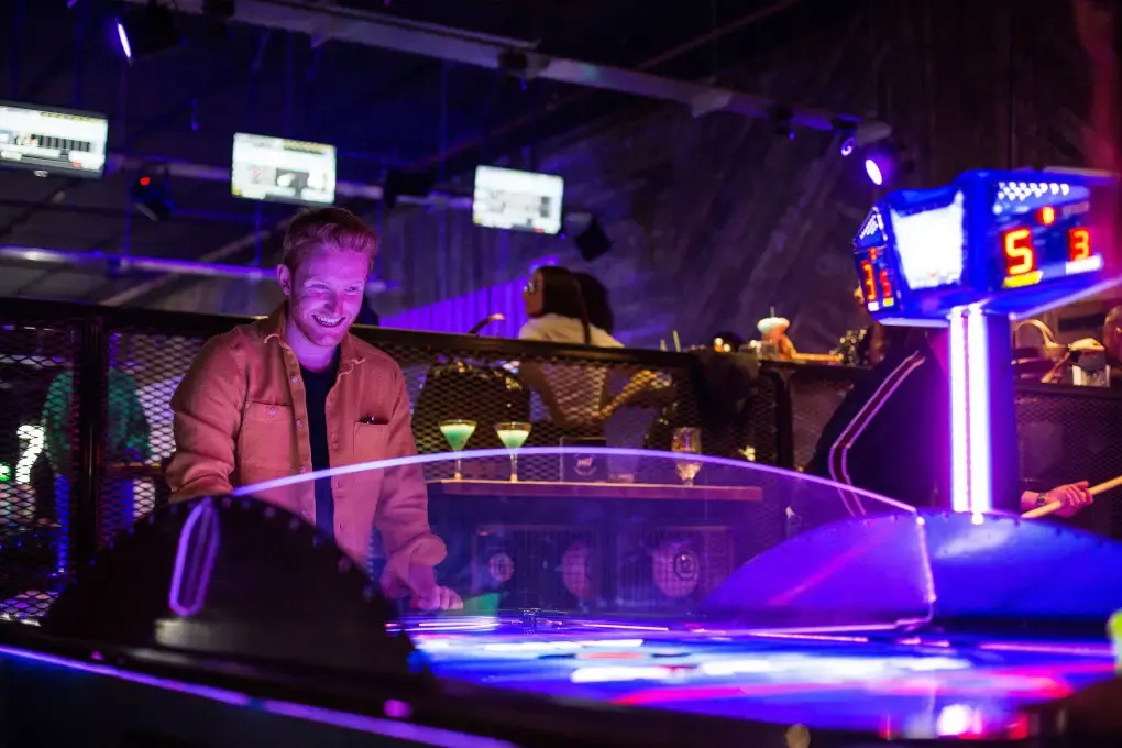 Young person playing air hockey under neon purple lighting in an indoor entertainment venue.