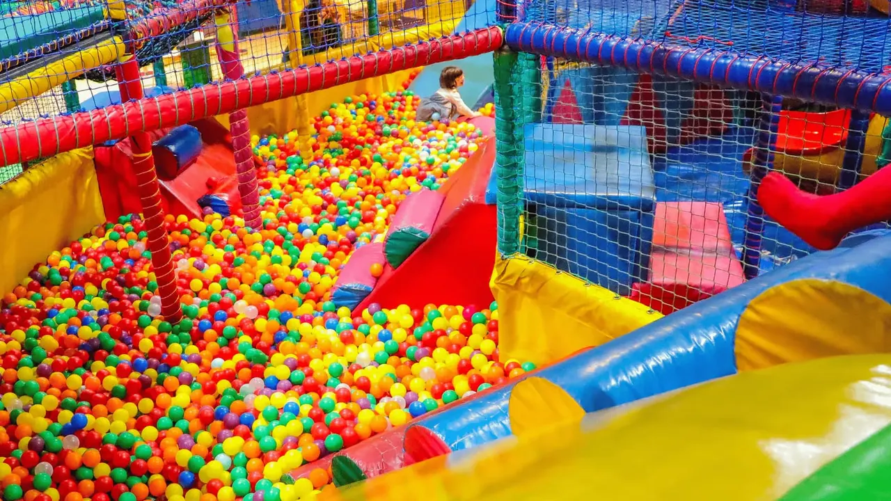 Child playing in a colourful ball pit within a large inflatable play structure.