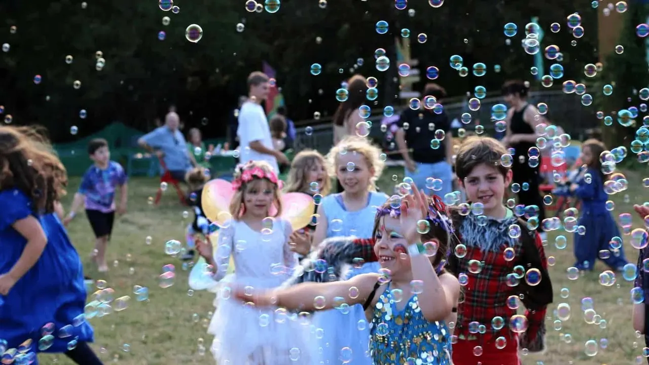 Children playing in a shower of soap bubbles at an outdoor garden event.