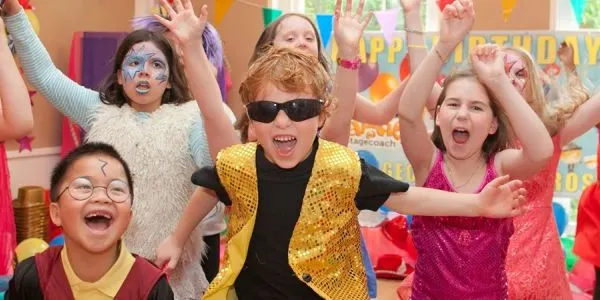Children in colourful outfits and face paint celebrate at a birthday party with decorations and balloons.