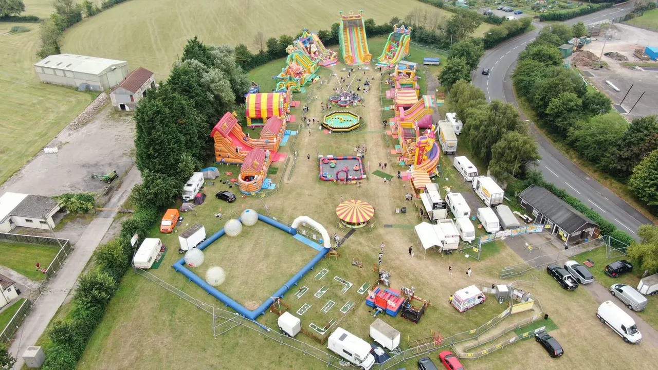 Aerial view of inflatable bouncy castles and slides set up in a field with visitors enjoying the attractions.