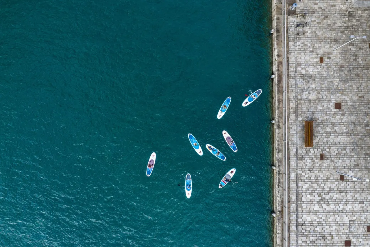 Aerial view of paddleboards moored in turquoise water next to a stone quay.