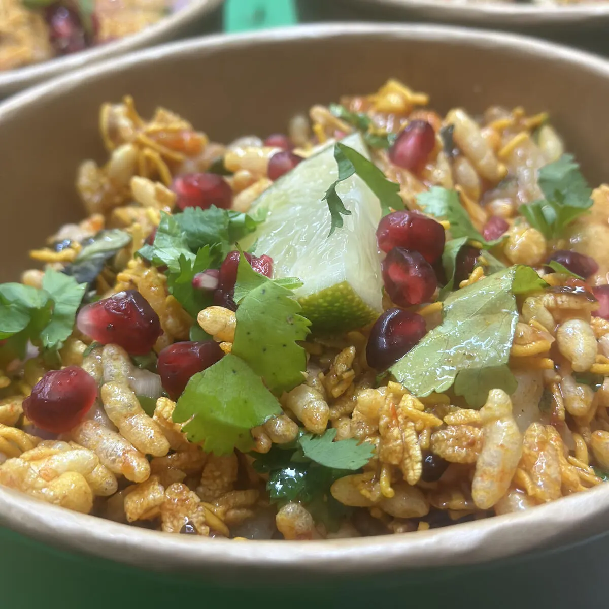 Bowl of lentil and grain dish garnished with pomegranate seeds, lime wedges and fresh coriander leaves.