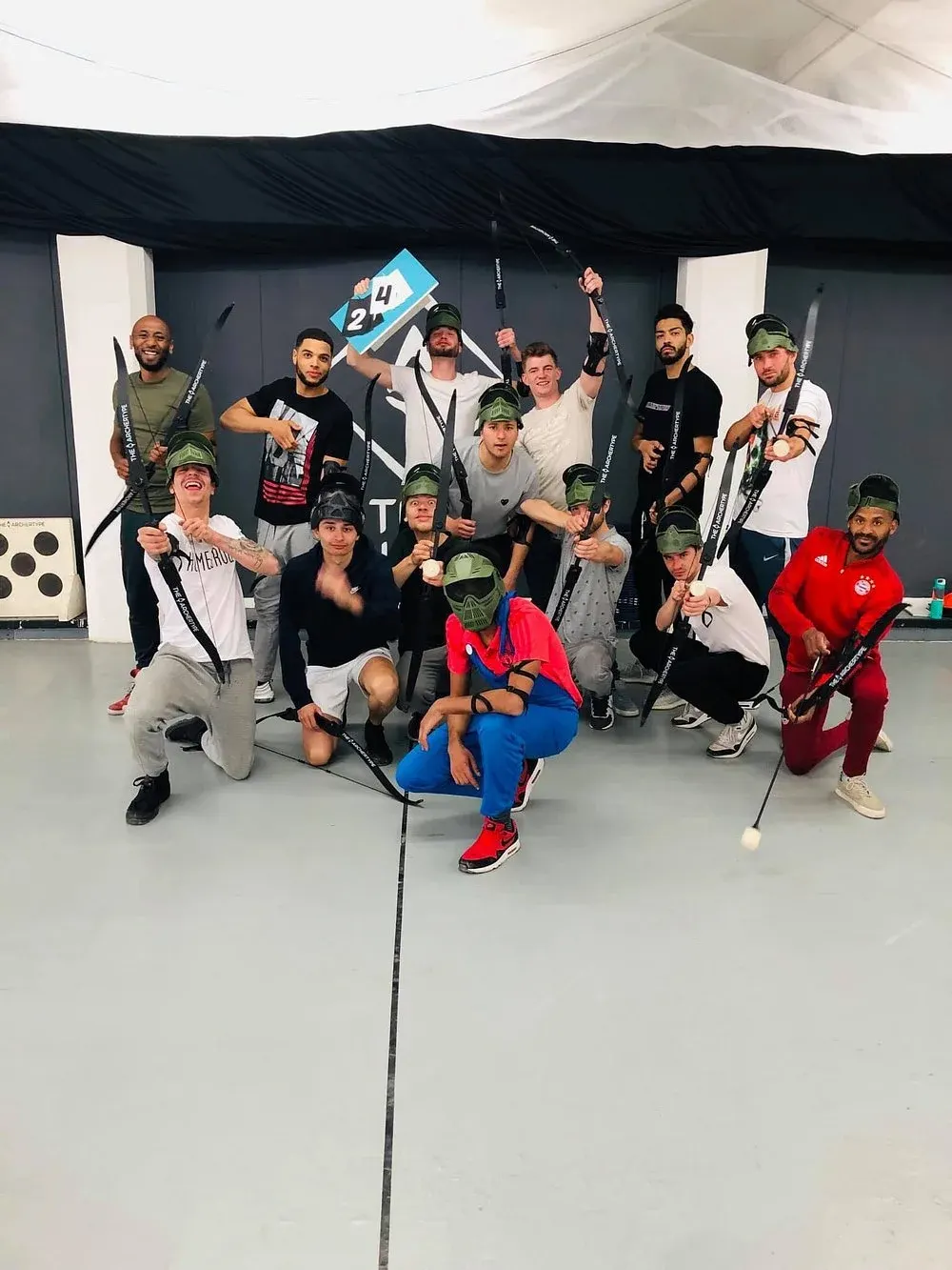 Large group of people posing together indoors whilst holding recurve bows and wearing protective eyewear and arm guards.