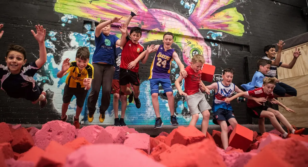 A group of children jumping and playing on red foam blocks in an indoor trampoline park with colourful butterfly wall art.