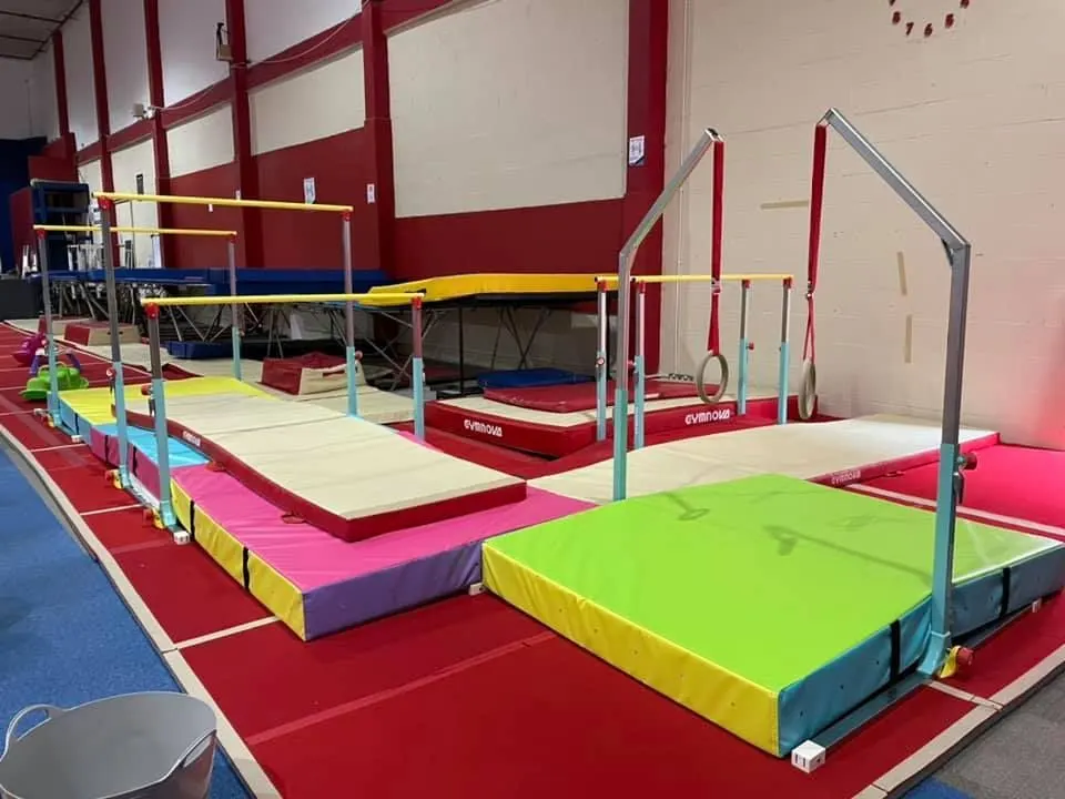Indoor gymnastics hall with colourful padded mats, bars and equipment set up for training.