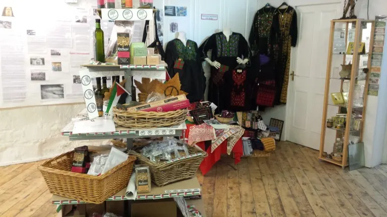 Interior display of Palestinian cultural artefacts, traditional clothing, and handicrafts in a museum shop setting.