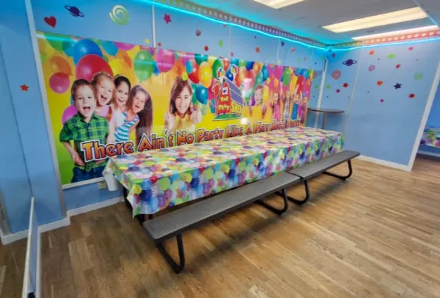 Colourful party room with themed wall graphics, decorated table and benches ready for children's celebrations.