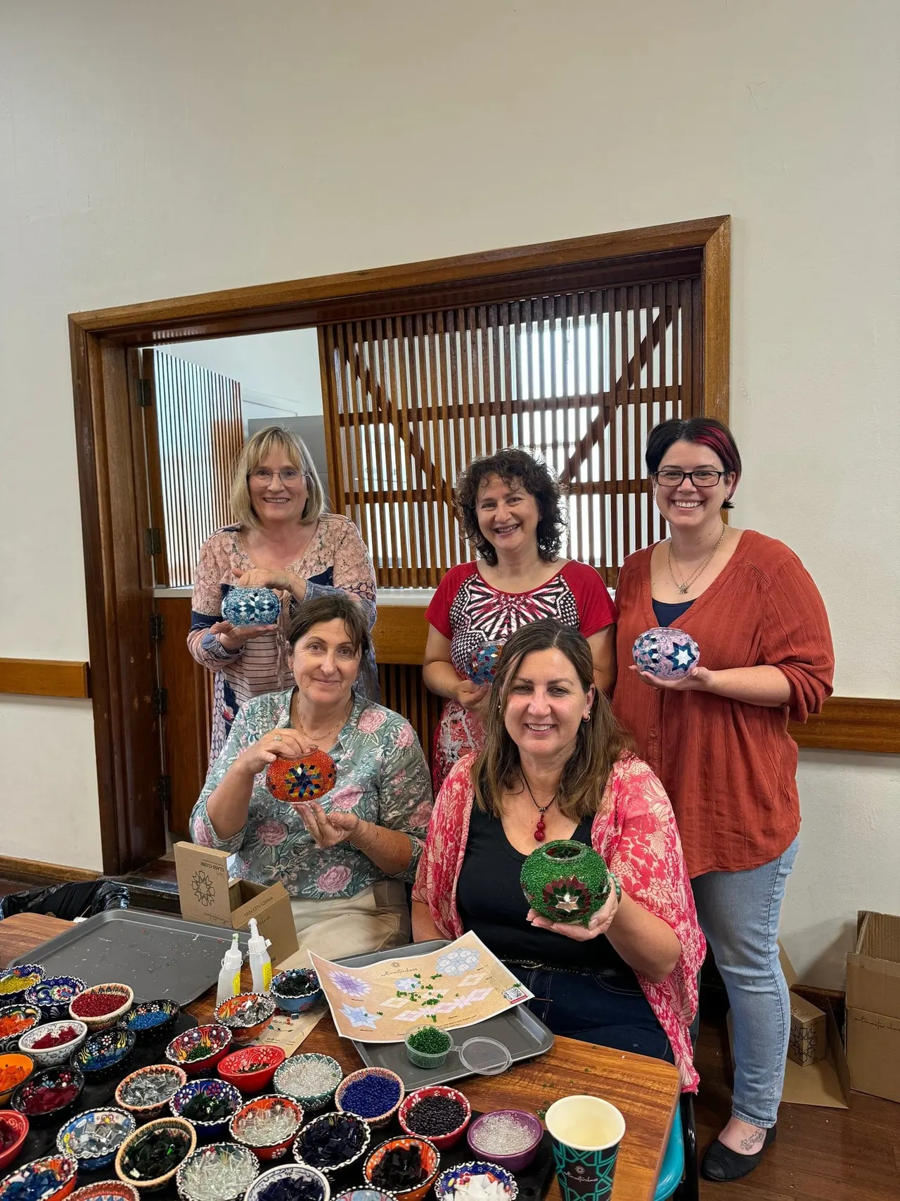 Five women displaying handmade decorative ceramic bowls at a craft workshop table.