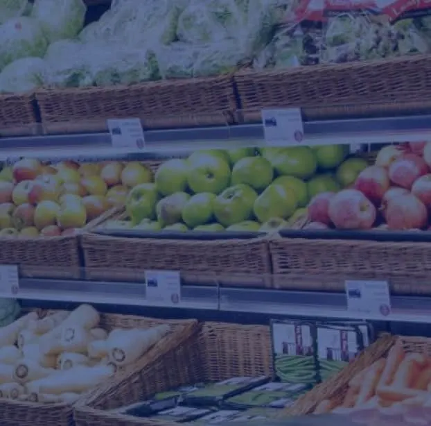 Wicker baskets of fresh produce including apples, lettuce and vegetables displayed on tiered shelving.