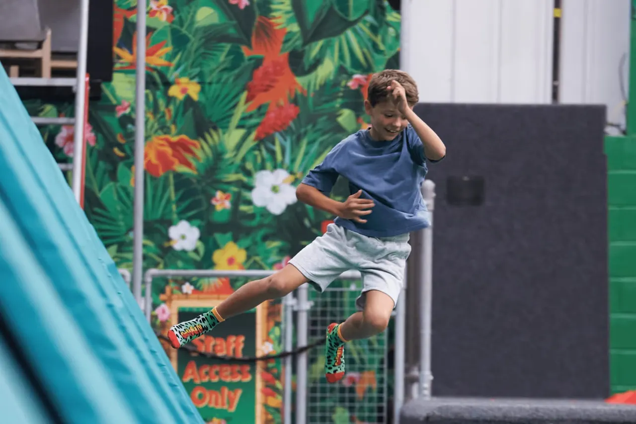 Young child jumping on a trampoline indoors with tropical flower artwork on the walls behind.