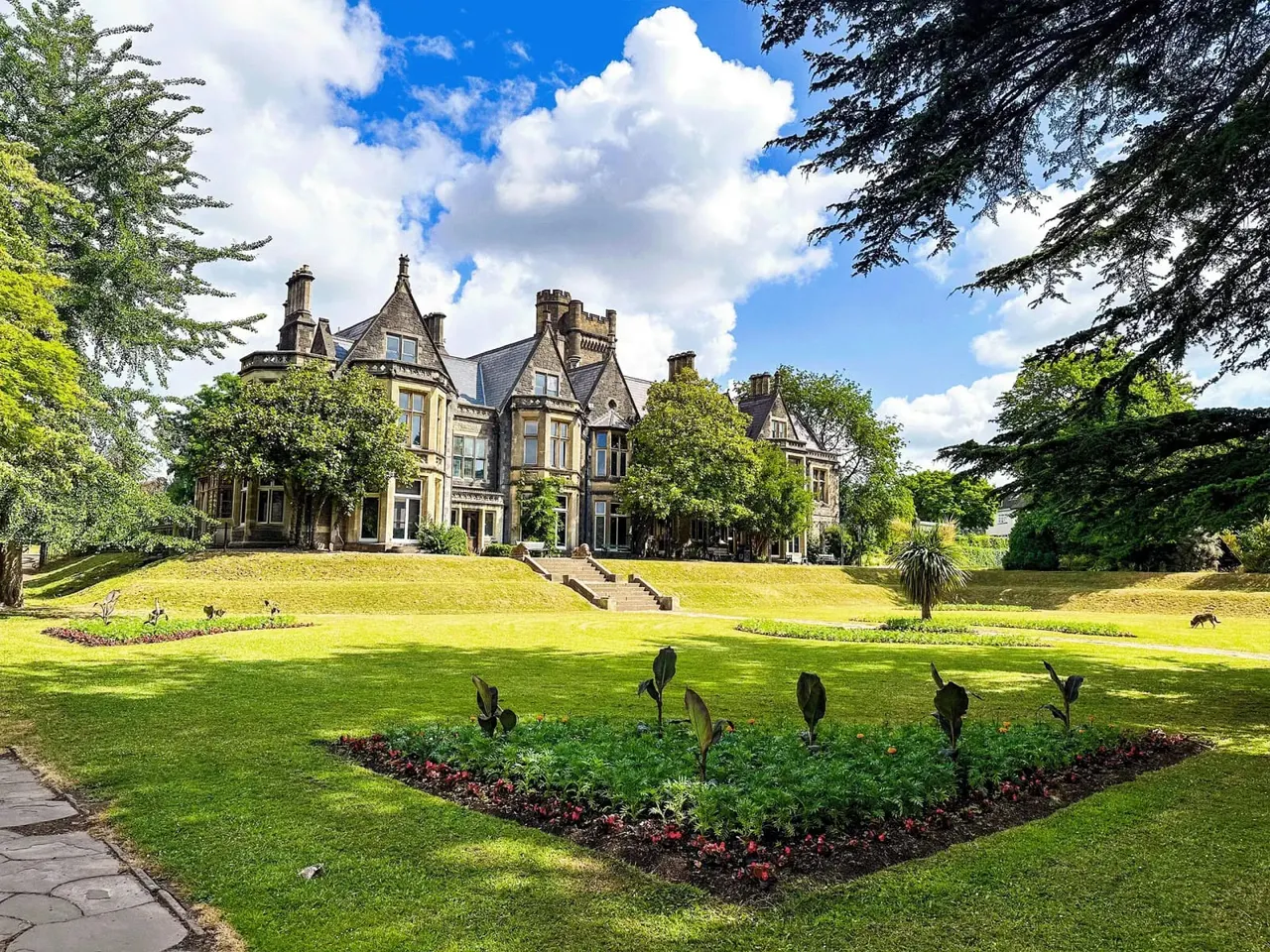 Victorian mansion with manicured lawns and garden beds containing large bird sculptures in the foreground.