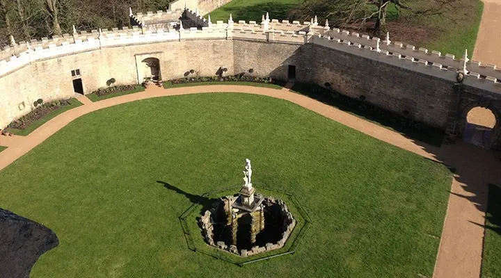 Aerial view of a circular grass courtyard with a central ornamental monument within a historic castle's defensive walls.
