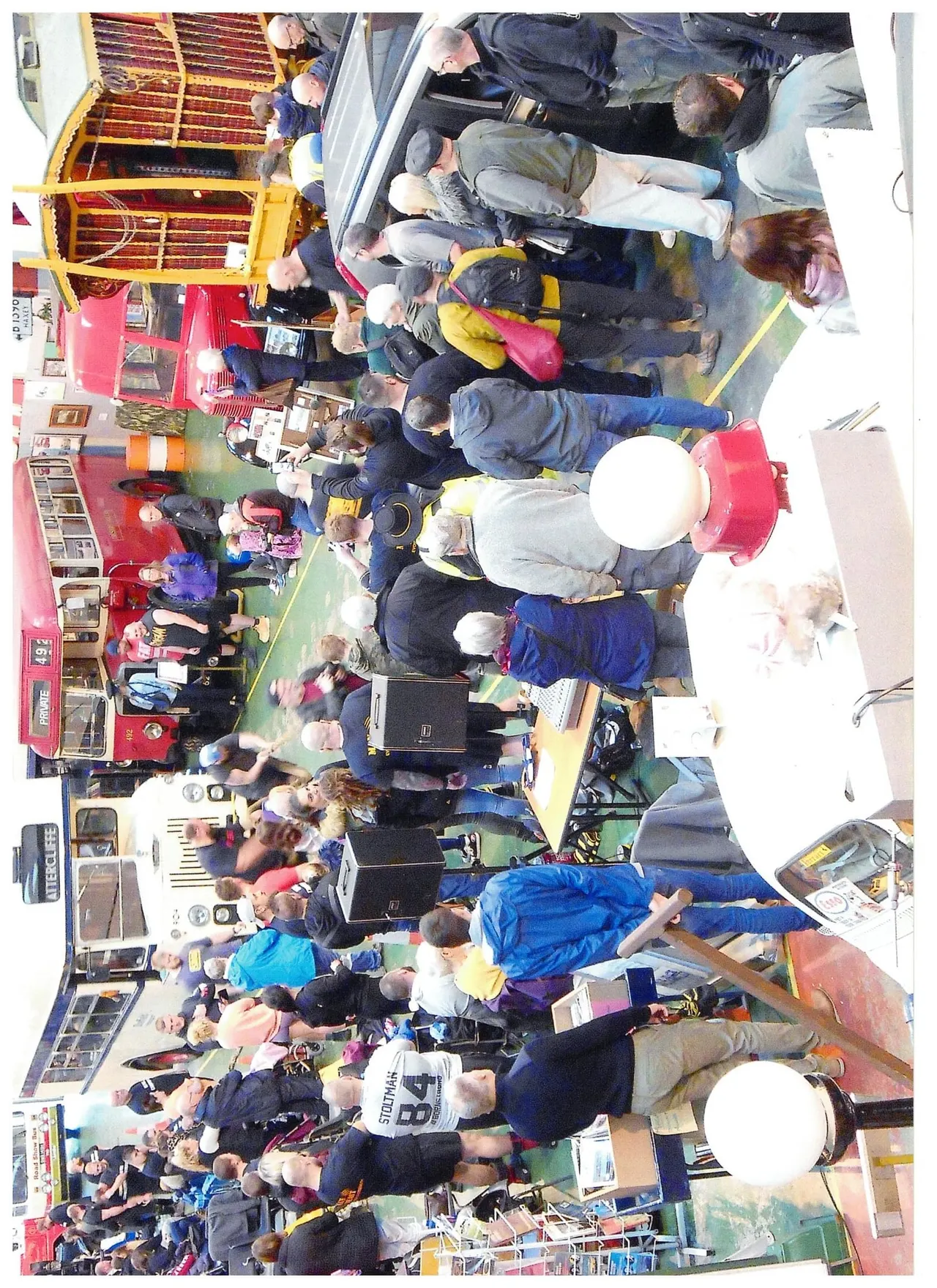 Overhead view of visitors exploring a red vintage bus interior and museum exhibition space with vintage vehicles and displays.
