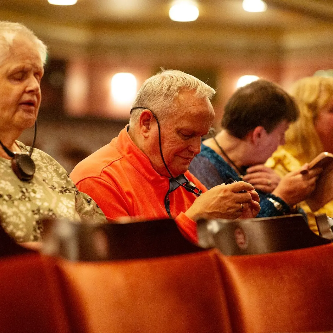 Older adults seated at a dining table with red tablecloth, enjoying a meal together indoors.