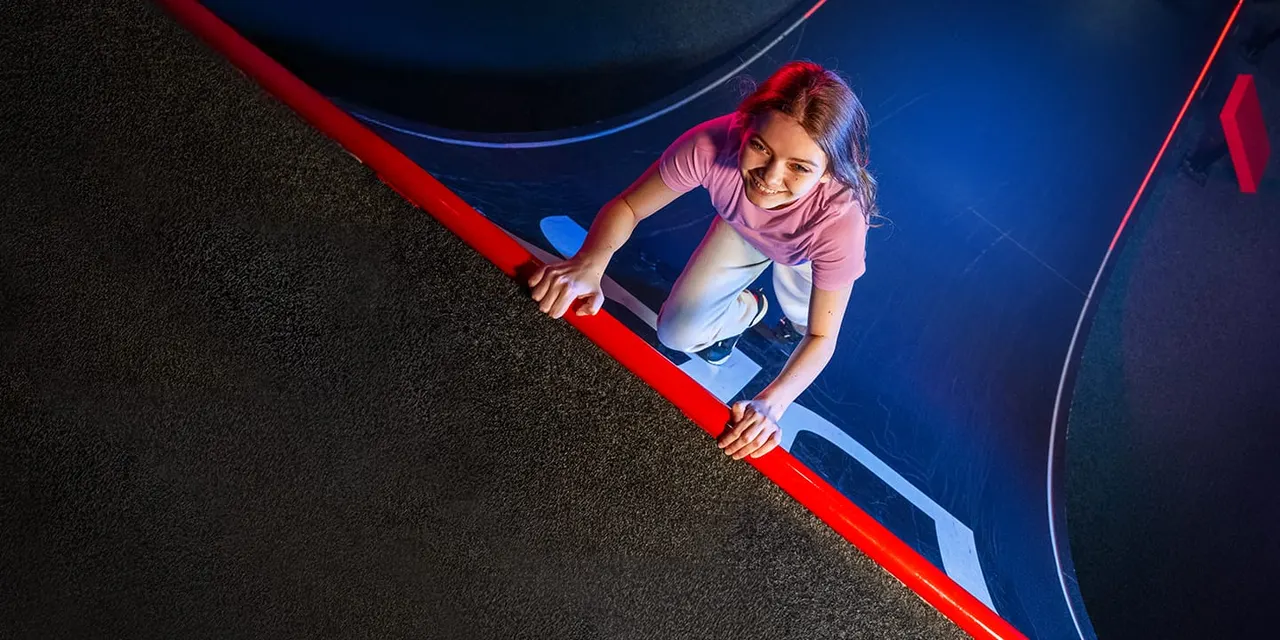 Child climbing a red rope obstacle course element indoors under blue lighting.