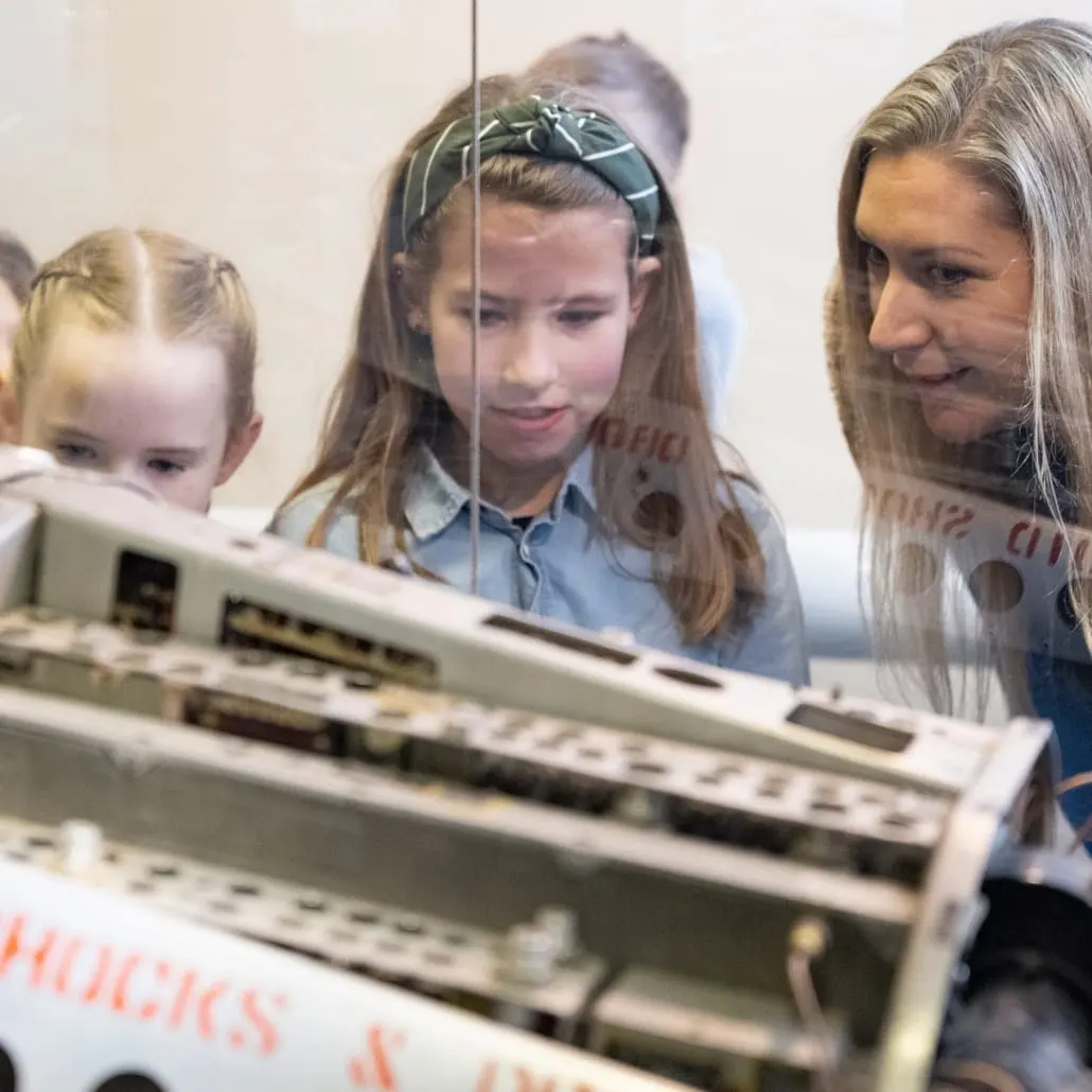 An adult and two children examine a vintage radar display system at an interactive museum exhibit.