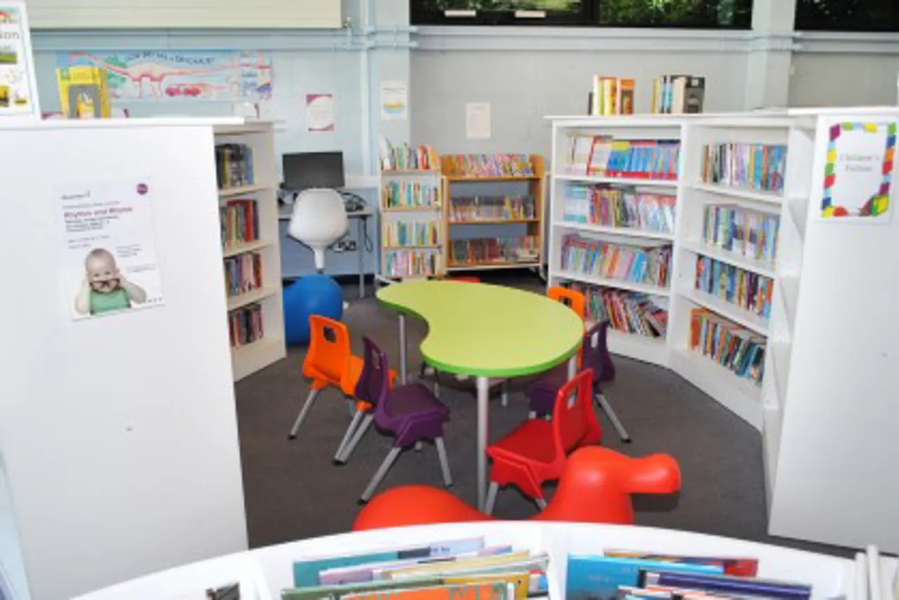Children's library area with lime-green table, colourful chairs, bookshelves, and bouncing toys on dark flooring.