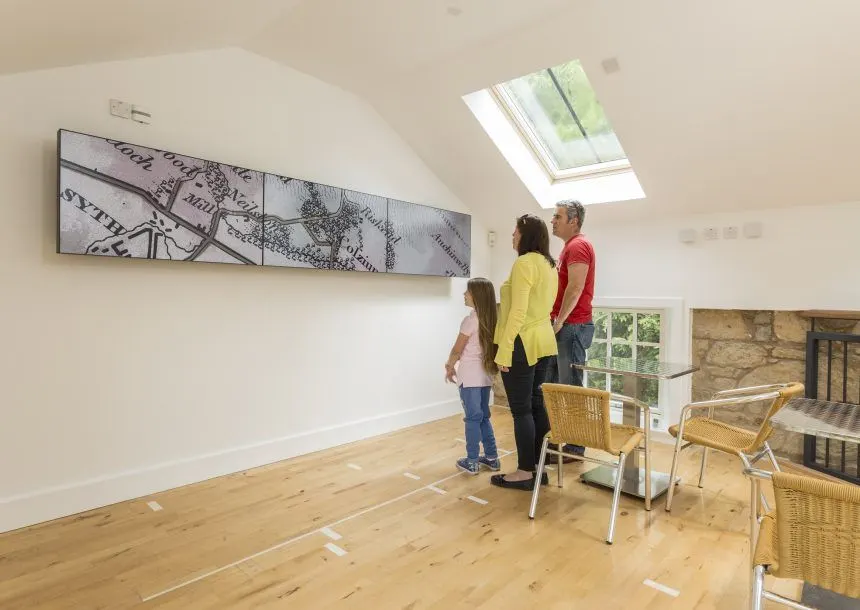 A woman and two children viewing wall art in a bright, modern gallery space with wooden flooring.