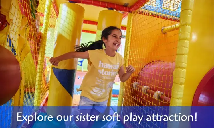A young child laughs while playing inside a colourful soft play structure with padded walls and netting.