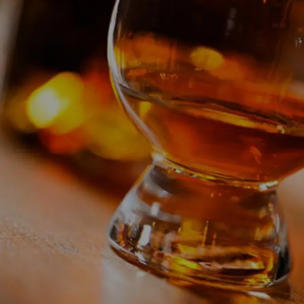 Glass of whisky with warm lighting in the background.