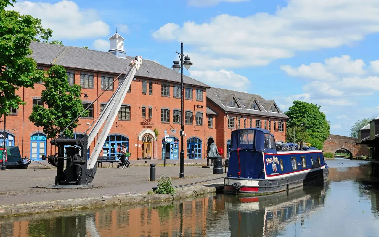 Canal narrowboat moored beside a red-brick building with vintage crane at a waterside leisure venue.