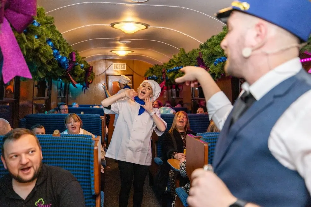 Performers in period costume entertain passengers inside a decorated vintage train carriage during a festive event.